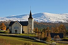 Foto einer weißen Holzkirche, dahinter eine verschneite Berglandschaft