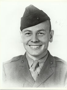 A young man dressed in his military uniform and wearing a Marine Corps style hat. He is smiling.