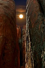 A full moon shining between the peaks of two sandstone towers in Arches National Park