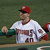 A Caucasian male, wearing a red baseball hat and white uniform with red lettering standing in a dugout