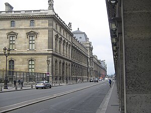 Le palais du Louvre, vu d’entre deux arcades de la rue de Rivoli. Celles-ci, à droite sur la photographie, sont du côté des numéros pairs.