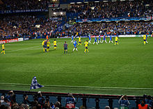 Chelsea (blue) and Barcelona players (yellow) leave the pitch at the end of the first half of their semi-final second leg at Stamford Bridge. The referee is talking to two Barcelona players.