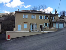 Mairie de Lambruisse, sur un terrain en pente. Le monument aux morts est construit sur une terrasse qui rattrappe le dénivelé devant le bâtiment