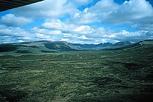 Vue aérienne en enfilade d'une large vallée en auge verdoyante et parsemée de petits lacs.