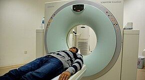 A person lying down, about to go through a CT scanner.