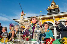 A middle-aged man and woman standing in front of some silver trophies with other people in the background