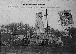 Photo noir et blanc montrant une grande tour en bois et son personnel au milieu d'un hameau.