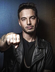 A foto mostra J Balvin de frente, com sua mão fechada apontada para a câmera, mostrando suas tatuagens.