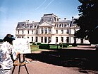 Photographie en couleurs d'un château qu'un artiste au premier plan est en train de peindre.