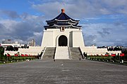 A white monument. A large alley surrounded by flags leads to it.