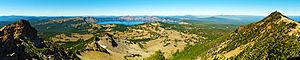 A panorama shot displays Crater Lake in the center background, with mountains in the foreground on the left and right