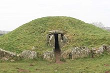 A law grassy mound wi an entrance at its centre framed bi cyclopean stones