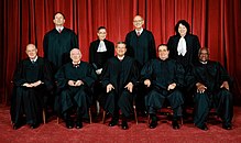 Nine judges in black robes pose for a photograph, four are seated, five stand behind them.