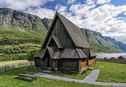 Foto einer hölzernen Stabkirche, im Hintergrund ein Bergmassiv und ein See