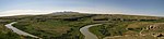 A small river winds through a rocky, grass-covered plateau. Hills rise in the distance.