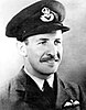 Head-and-shoulders portrait of a Caucasian man in dark tie, light shirt, and dark jacket with pilot's wings on left-breast pocket, wearing peaked cap