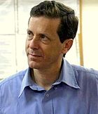 Man with dark hair, wearing a blue shirt, photographed from the shoulders up, looking to his right.