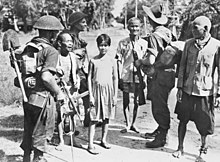 Soldiers carrying packs talk to civilians on a jungle road