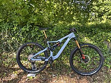 Ein blaues, vollgefedertes Enduro MTB steht vor einer Hecke