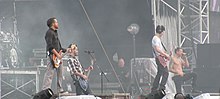 A color photograph of members of the group Linkin Park performing on and outdoor stage