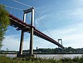 Pont suspendu aux piliers gris et tablier rouge au-dessus d'un fleuve.