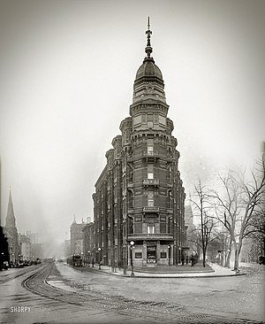 An ornate, wedge-shaped apartment building with six floors. At the corner is a turret topped with a spired cupola.