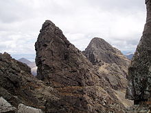 Rugged mountain scenery - several sharp prominences of bare grey rock stand out on a long ridge leading to more hills beyond.