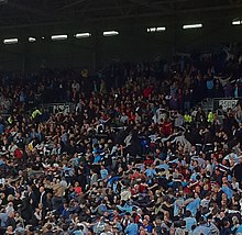 Photo des supporters de Manchester City, en tribune dos tourné au terrain, effectuant la danse du Poznań.