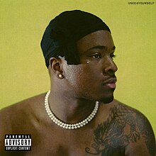 A shot of a shirtless IDK wearing a do-rag and looking sideways on a yellow background