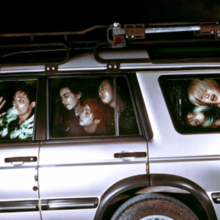 The members of P1Harmony in a silver station wagon with their faces pressed up against the windows