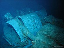 The mangled wreck of a naval gun turret. The photograph has a blue tinge, as it was taken in deep water.