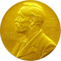 A golden medallion with an embossed image of a bearded man facing left in profile. To the left of the man is the text "ALFR•" then "NOBEL", and on the right, the text (smaller) "NAT•" then "MDCCCXXXIII" above, followed by (smaller) "OB•" then "MDCCCXCVI" below.