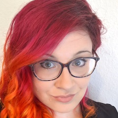 Close up of a smiling light-skinned woman wearing glasses with long red hair.