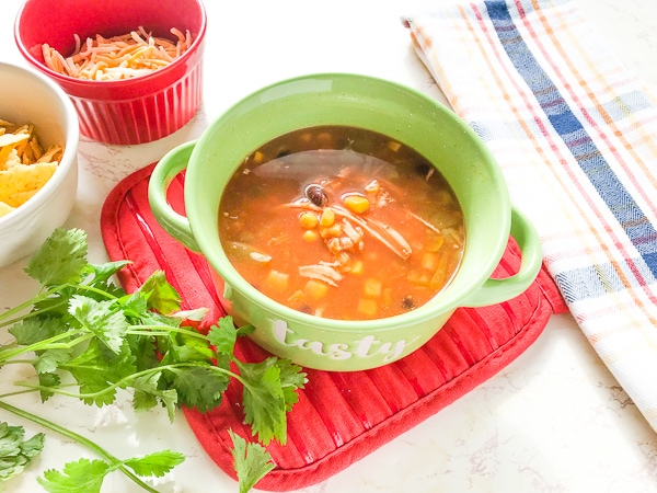 A green soup bowl filled with the instant pot chicken tortilla soup recipe next to a bunch of fresh cilantro.