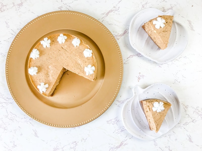 Overhead shot of instant pot pumpkin cheesecake on a gold plate next to two slices on pumpkin plates.