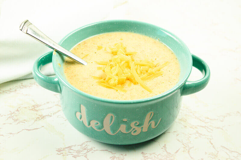 A teal bowl filled with broccoli cheese soup.