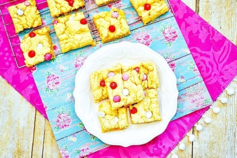 A pink tablecloth topped with a floral placemat with a cooling rack of cookie bars and a white plate of cookie bars on top!