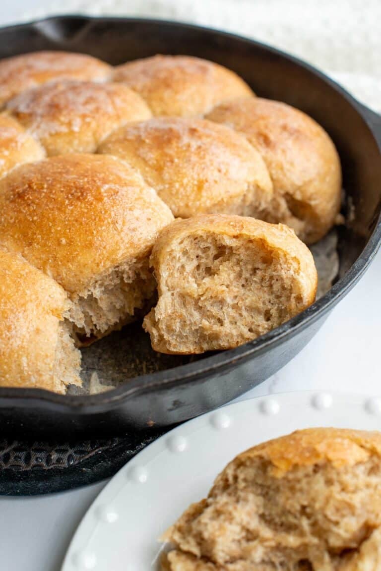 Honey whole wheat dinner roll in a skillet with other dinner rolls - leaning on its side to show the airy crumb.