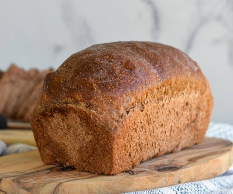 Loaf of sourdough discard brown bread sitting on a board with slices of brown bread behind it.