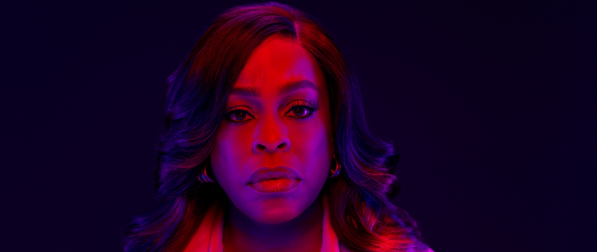 Niecy Nash as Lois Tryon wearing a light trench coat under neon lights