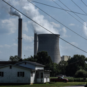 A house is in the foreground of two smokestacks that are emitting plumes.