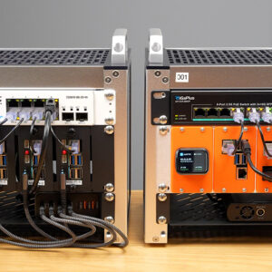 Two mini-racks in cube-style silver containers, one with an orange back and the other silver, on a wooden desk, ethernet cables neatly fanning out from each.