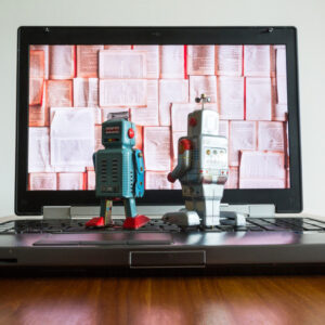 Two tin toy robots looking at laptop screen.