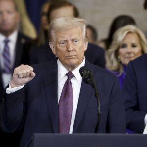 US President Donald Trump holds up his right hand in a fist after being sworn in at his inauguration on January 20, 2025 in Washington, DC. Former President Joe Biden stands behind Trump.