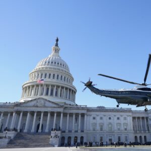 A helicopter with the words "United States of America" and a US flag lifts off in front of the US Capitol building