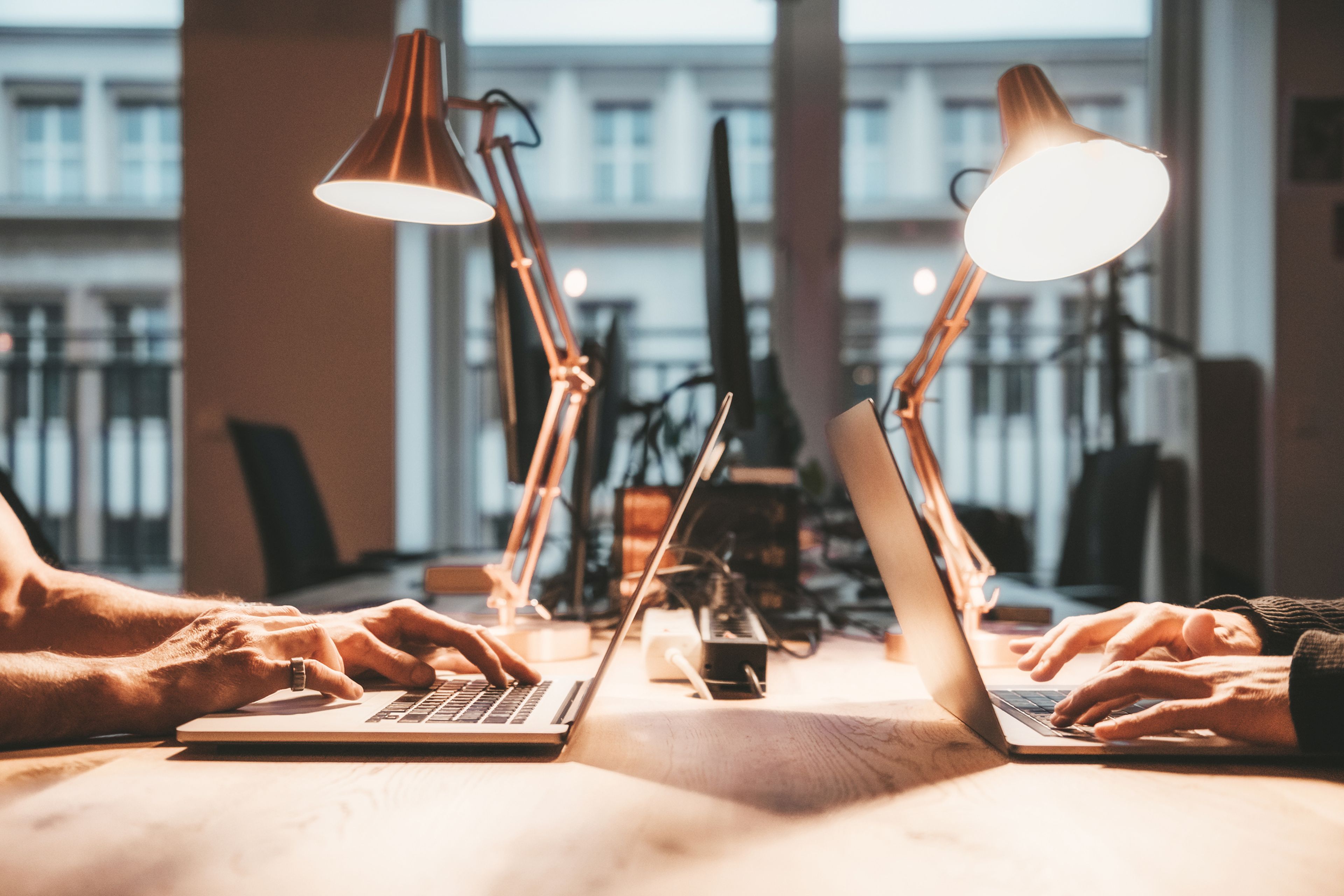 2 personas trabajan con 2 ordenadores a la luz de los flexos.