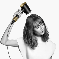 black and white image of woman with short hair drying hair with dyson limited edition onyx and gold supersonic dryer 