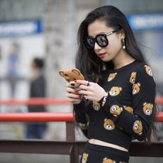 Lady wearing big sunglasses and a teddy bear sweater looking at her phone