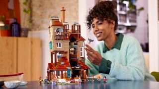 Lego The Burrow set and minifigures on a table, with a woman holding a mini owl in the background