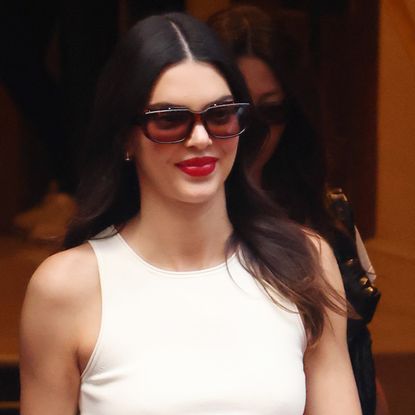 Kendall Jenner between shows at Paris Couture Week wearing tinted sunglasses red lipstick and a white tank top